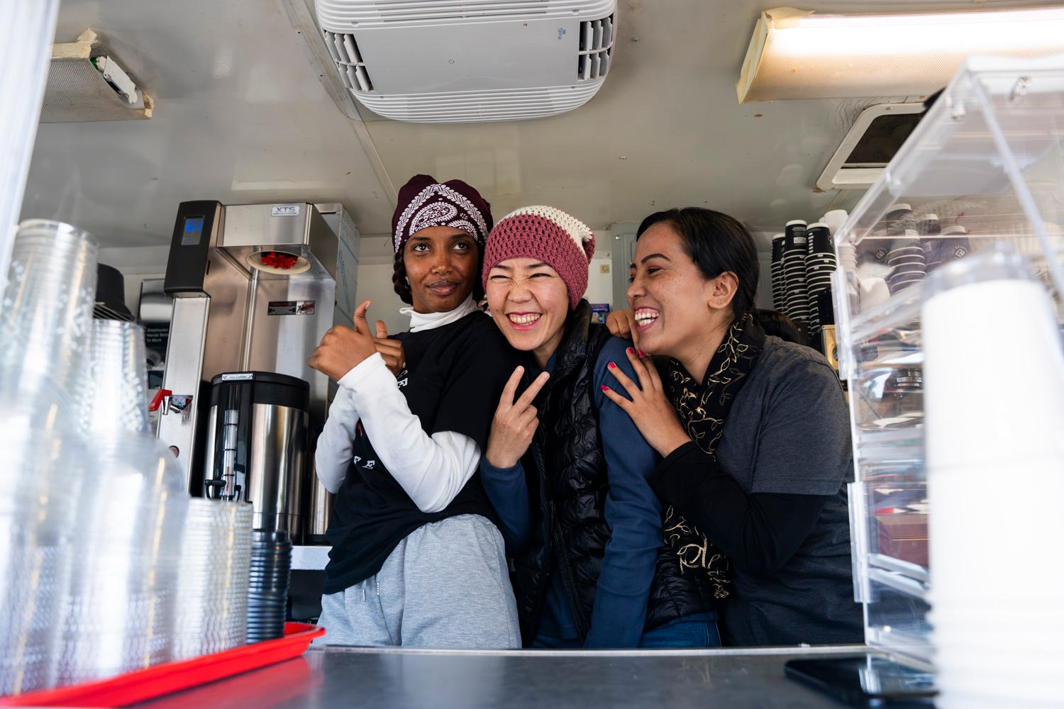 Three women working in a coffee truck having fun